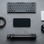 A flat-lay photography of a smartphone surrounded by a foldable keyboard, a sleek power bank, small wireless earbuds, and a compact tripod on a modern desk.