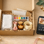 Open DIY craft kit box with clay, watercolor paints, brushes, embroidery thread, candle jar, instruction cards, and smartphone tutorial.