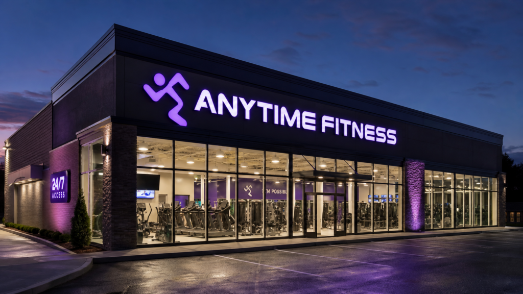 Exterior view of a modern Anytime Fitness gym at night, with the iconic purple logo illuminated, showcasing the 24/7 franchise model.