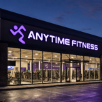Exterior view of a modern Anytime Fitness gym at night, with the iconic purple logo illuminated, showcasing the 24/7 franchise model.
