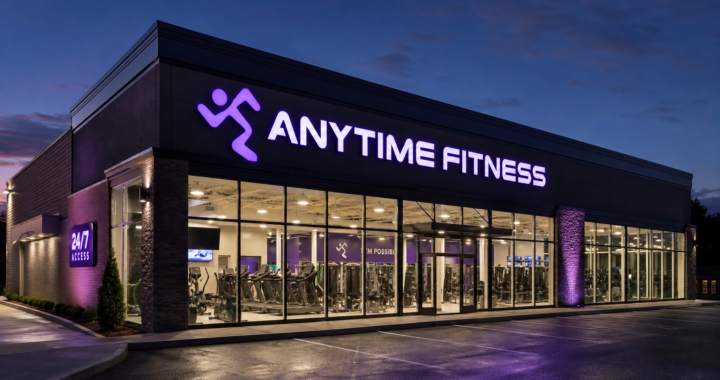 Exterior view of a modern Anytime Fitness gym at night, with the iconic purple logo illuminated, showcasing the 24/7 franchise model.