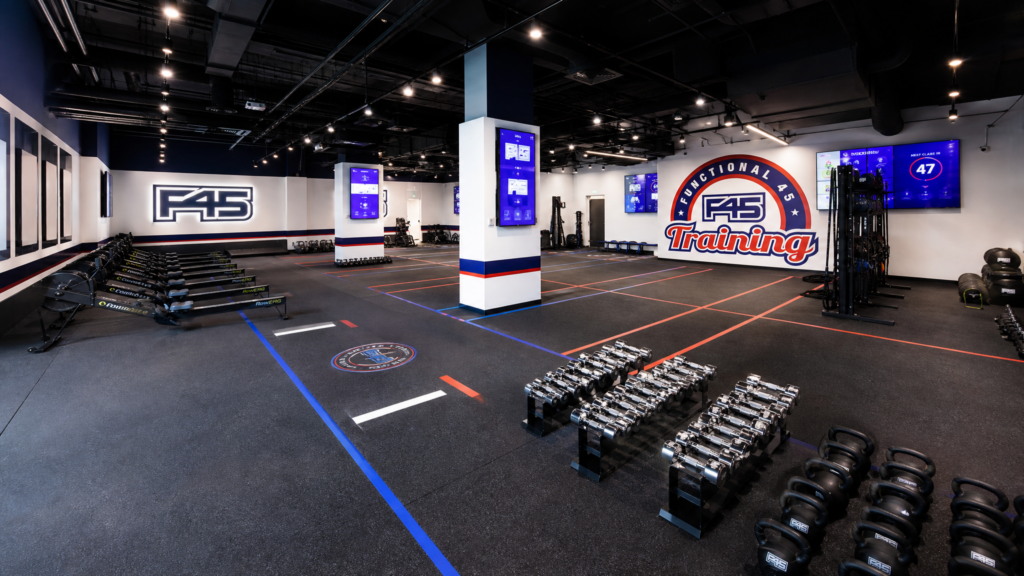 Modern F45 Training studio interior featuring blue, red, and white equipment, digital screens showing workouts, and a clean, high-energy functional training floor.