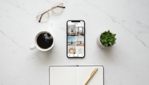 A top-down lifestyle shot of a smartphone on a clean white desk, showing a Pinterest-inspired aesthetic with a coffee cup and a small plant.