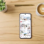 A high-end smartphone on a light oak desk showing a Pinterest 'Dream Life' board with affiliate sales charts.