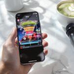 A smartphone held in a clean hand over a marble desk showing a TikTok short-form video editor and a graphic vertical conversion funnel next to a matcha latte and a wireless mic.