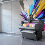 A high-tech vertical wall printing machine printing a colorful abstract geometric mural on a concrete office wall with floor rails.